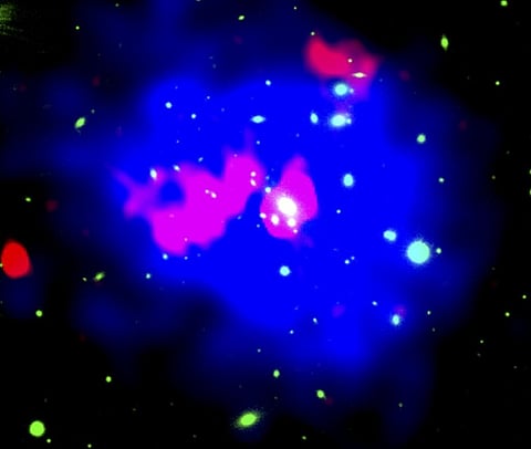 Optical photograph of the cluster of galaxies, whose central giant elliptical galaxy (white elliptical patch) is the parent of the radio lobes shown in red. The blue shaded region displays the halo of X-ray emission due to the hot gas associated with this cluster of galaxies and have an overall size of around 1.7 million light-years.