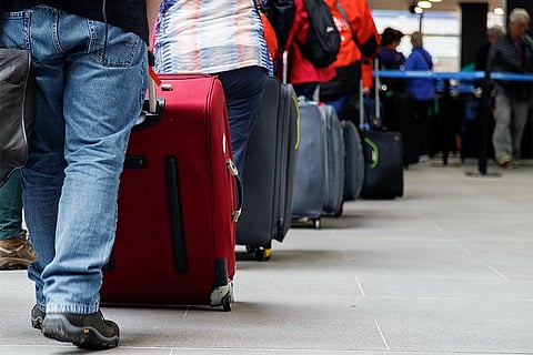 हवाई अड्डे के चेक-इन काउंटर पर सामान के साथ इन्तजार करते प्रवासी; फोटो: आईस्टॉक