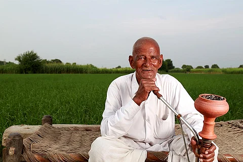 अपने खेतों के पास हुक्का पीता किसान; फोटो: आईस्टॉक
