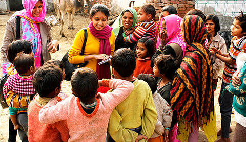 Two female social workers are interacting with a group of villagers comprising of children and female adults
