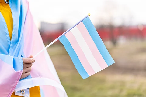 A person covered with the transgender flag and holding a smaller transgender flag in their hand.