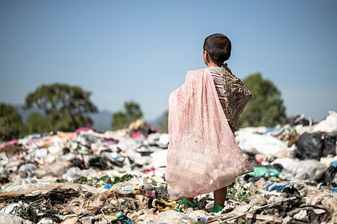 Rear view of child Standing on garbage dump with a sack in his hands