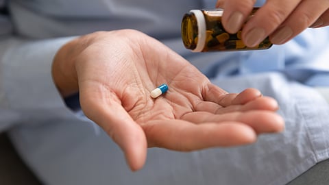 Close up of hands taking out blue and white pill from glass bottle