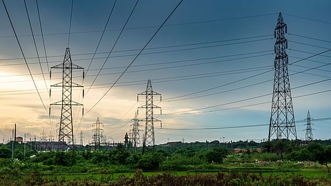 High voltage electric lines in the bush overlooking a power plant industry at sunset.
