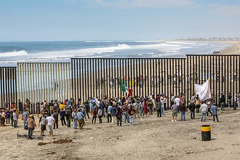 Migrants and workers gather on both sides of the iron and steel wall that separates the border between Mexico and the United States in Playas de Tijuana.