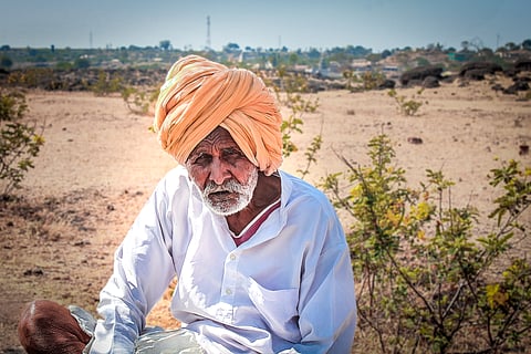 A old tired farmer sitting by the field taking a break from work.