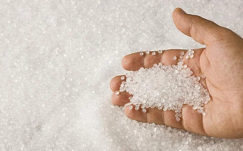 A hand sifting through a pile of clear plastic resin pellets. Photo: iStock