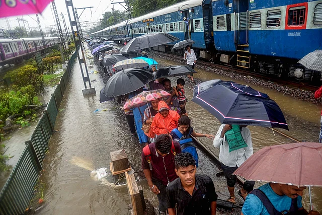 मुंबई में भारी बारिश से हाल बेहाल, पटरी से गुजरते यात्री