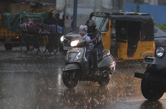 हैदराबाद में बारिश में स्कूटी पर पन्नी से सिर ढककर स्कूल जाता एक बच्चा.