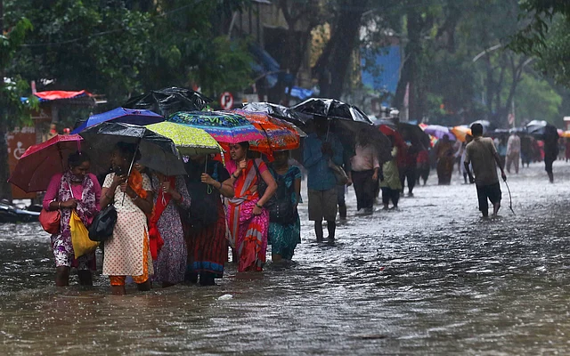 मुंबई में बारिश के दौरान एक जल भरी सड़क से गुजरते हुए लोग