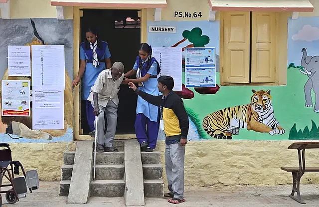बैंगलुरू में एक मतदान केंद्र पर अपना वोट डालकर बाहर आते एक बुजु्र्ग शख्स की मदद करते स्वयंसेवक 