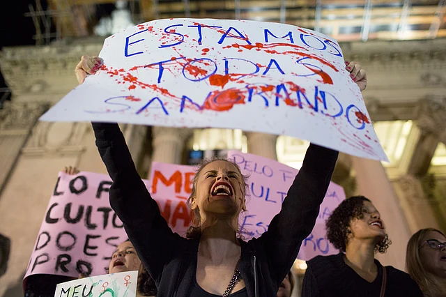 A woman shouts holding a banner that reads in Portuguese “We’re all bleeding” as she protests the gangrape. (Photo: AP)
