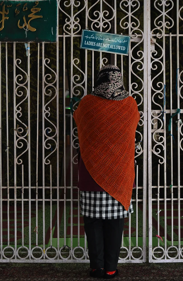 A woman prays outside Hazarat Bal Shrine on new year day as the board on the gate reads, ‘women are not allowed.’