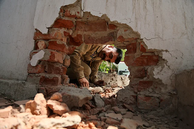 An Indian policeman looks at a hole made in a wall of a police station caused by a mortar shell.