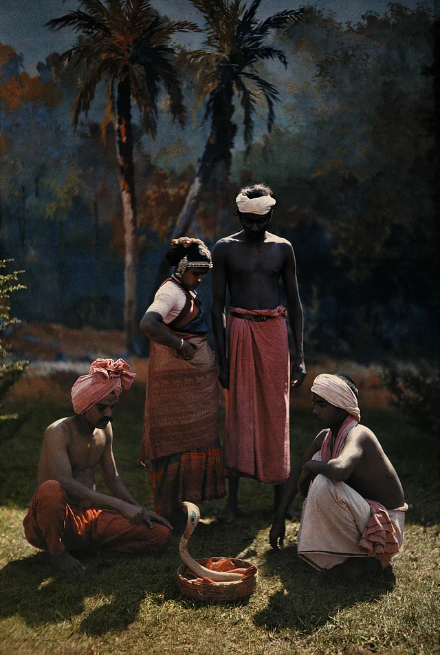 A group of people gather round and watch a snake charmer at work in India, 1923.