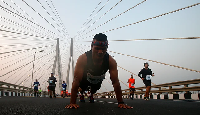 A participant does push-ups as other runners compete along the Bandra-Worli sea link over the Arabian Sea during the Mumbai Marathon on 20 January 2019. 