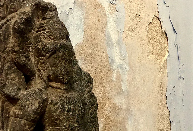 A sculpture of a demigod near the Amaravati section. The wall in the background is seeping and falling apart.