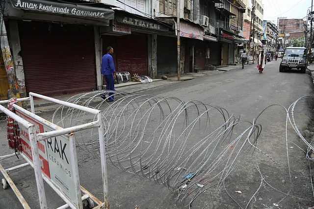 A pedestrian walks past a barbwire barricade set up by security officers.
