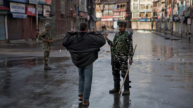An Indian paramilitary soldier orders a Kashmiri to lift his robe before frisking him during curfew in Srinagar.