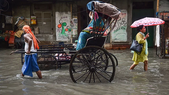 A hand rickshaw puller carries a passenger as another woman passes through a waterlogged street, following monsoon rain, in Kolkata on Thursday, 8 August.