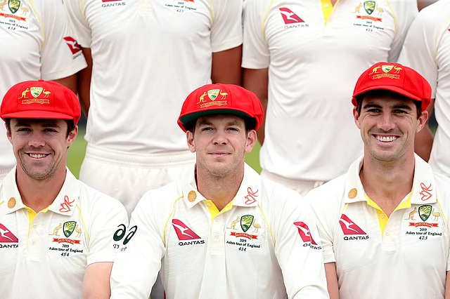 Australia’s Tim Paine centre, Travis Head, left and Pat Cummins pose for a team photograph wearing the red caps which will be worn on day two of the second Test.