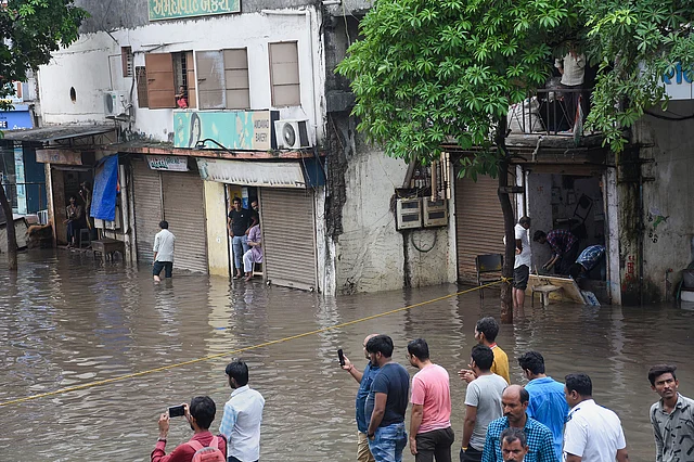 People look on at a waterlogged street where floodwater spilled out of the drainage line following heavy rainfall in Surat, on 10 August 2019.