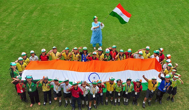 School students spread out a Tiranga as their teacher waves a flag during preparations for Independence Day.