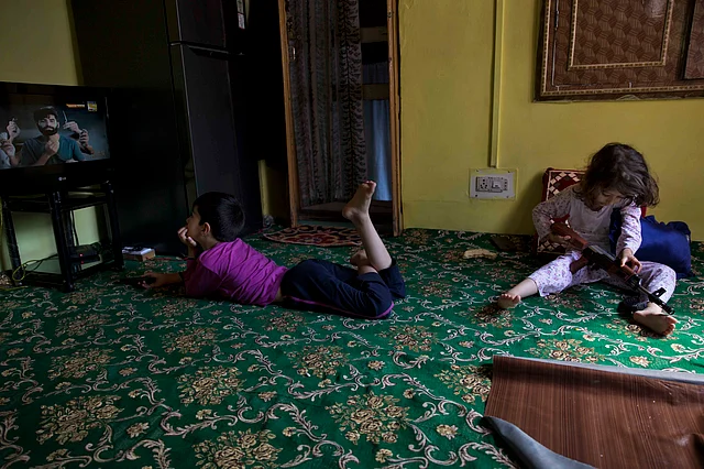 A Kashmiri boy watches television as his sister plays with a toy gun at home, in Srinagar.