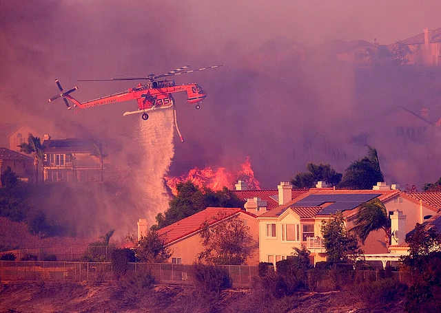 A skycrane makes a water drop on flames during between homes in Porter Ranch, California.
