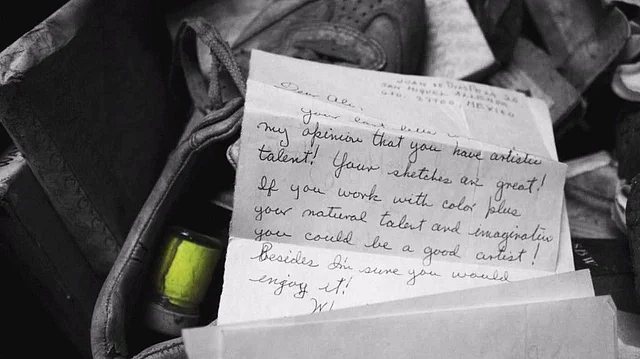 A letter addressed to Ali, appreciating his art, lies next to a crate full of old paint.