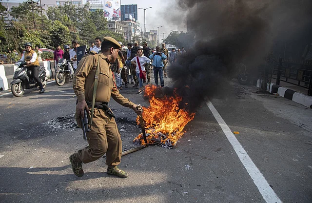 A policeman tries to douse a fire set by protestors against the Citizenship Amendment Bill (CAB) in Guwahati.
