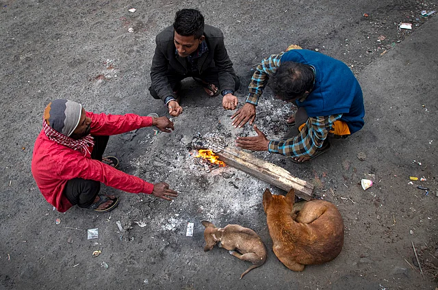 Daily wage labourers sit around a bonfire to keep themselves warm on a cold winter morning in Gauhati, India, Friday, 3 Jan 2020.