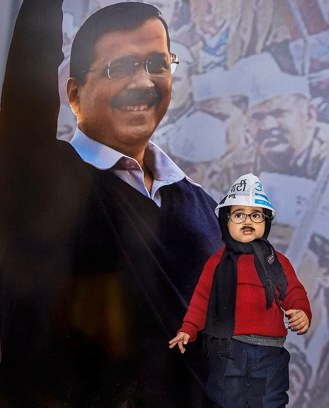 A young boy dressed as AAP’s Arvind Kejriwal stands in front of the CM’s hoarding as celebrations begin at party headquarters ahead of the Delhi Assembly polls results, in New Delhi.