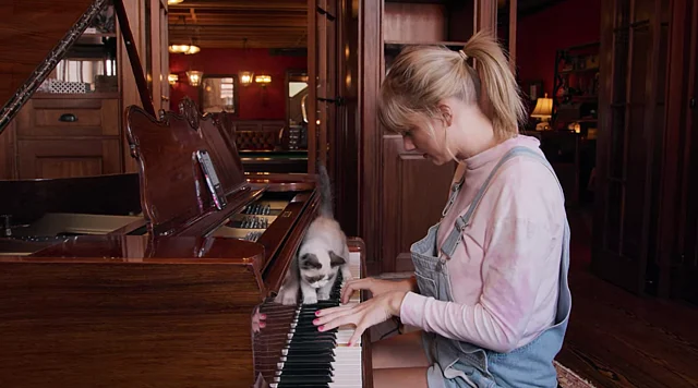 Taylor playing the piano, with her cat by her side.