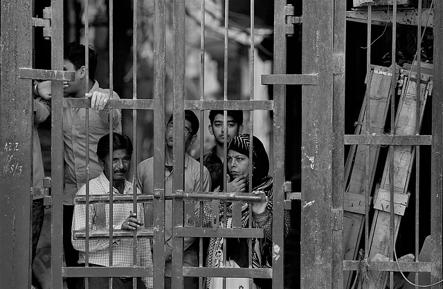 Residents look from behind a closed iron gate of their alley in Karaval Nagar two days after violence.