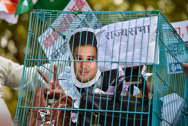 A Congress party worker wears a mask depicting former party leader Jyotiraditya Scindia and sits in a cage during a demonstration, in New Delhi, Wednesday, 11 March 2020.