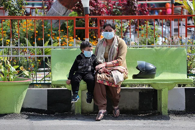 An Indian woman and a child wearing masks sit outside Government Medical College hospital in Jammu, India, Sunday, March 8, 2020.