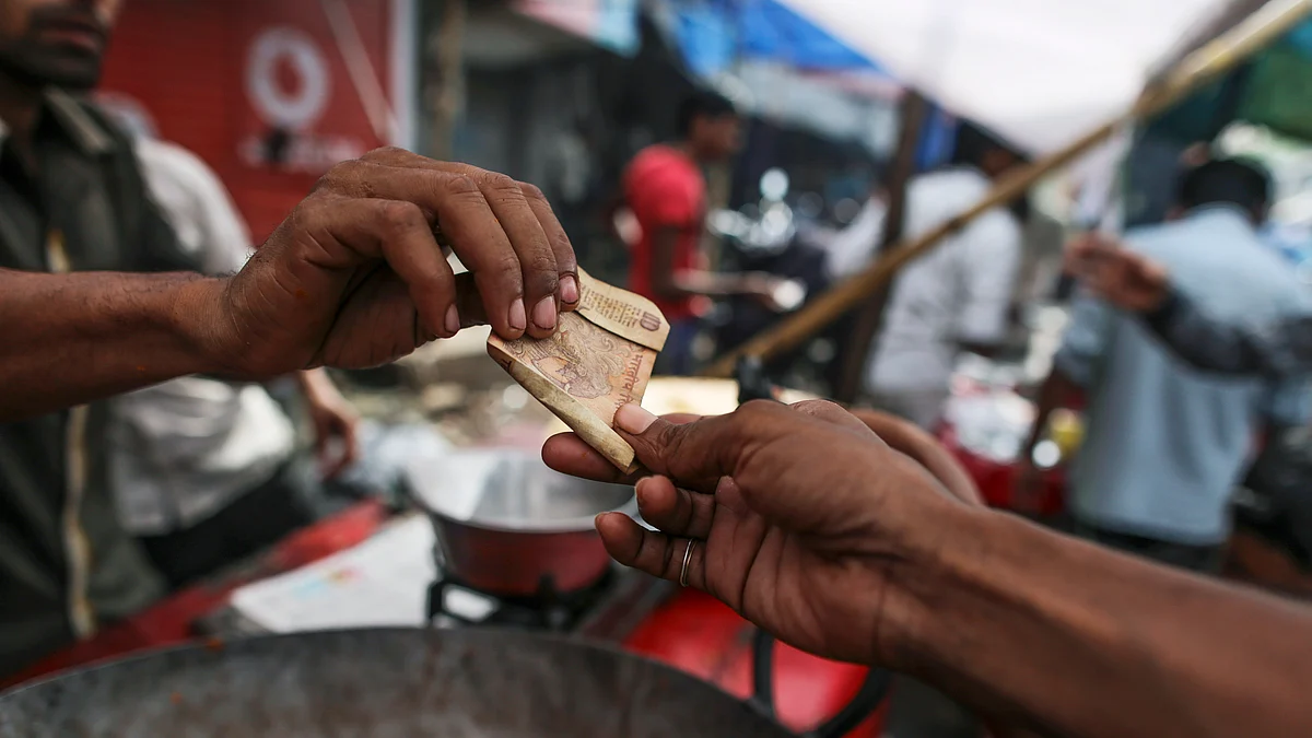 A customer hands an Indian ten rupee banknote to a snack vendor at a roadside stall in the Dharavi slum area of Mumbai (Photographer: Dhiraj Singh/Bloomberg)