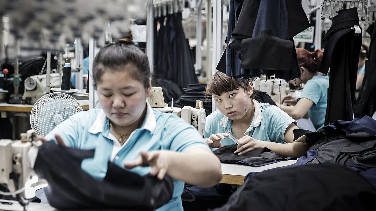 Employees place suit jackets in plastic covers at a factory (Photographer: Qilai Shen/Bloomberg)