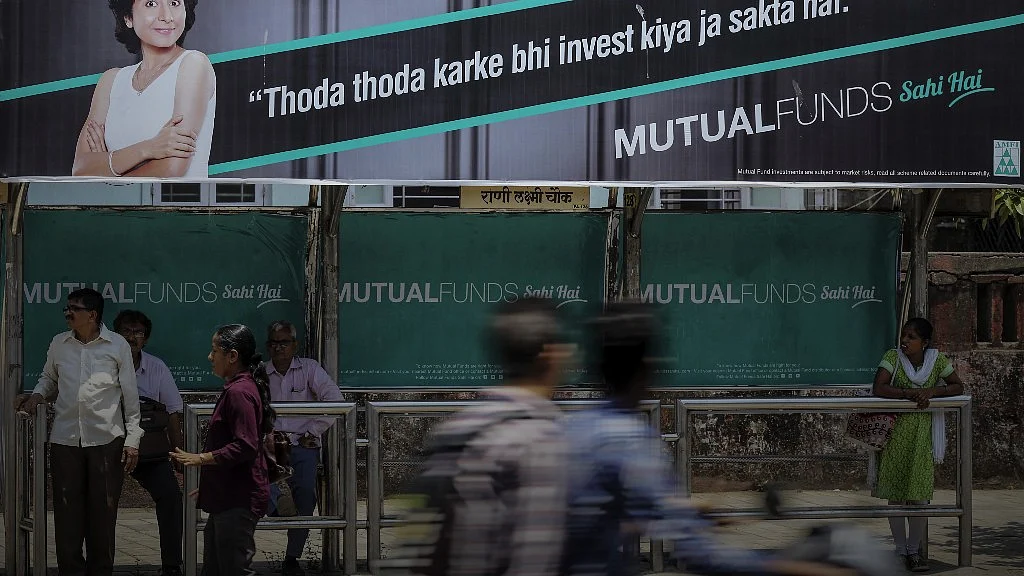 Pedestrians walk past passengers sitting next to an advertisement for the Mutual Funds Sahi Hai campaign by the Association of Mutual Funds in India at a bus stop in Mumbai, Maharashtra. (Photographer: Dhiraj Singh/Bloomberg)