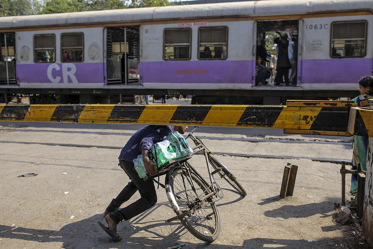A cyclist ducks underneath the barrier of a railway crossing as a train travels past near Sewri railway station in Mumbai. (Photographer: Dhiraj Singh/Bloomberg)