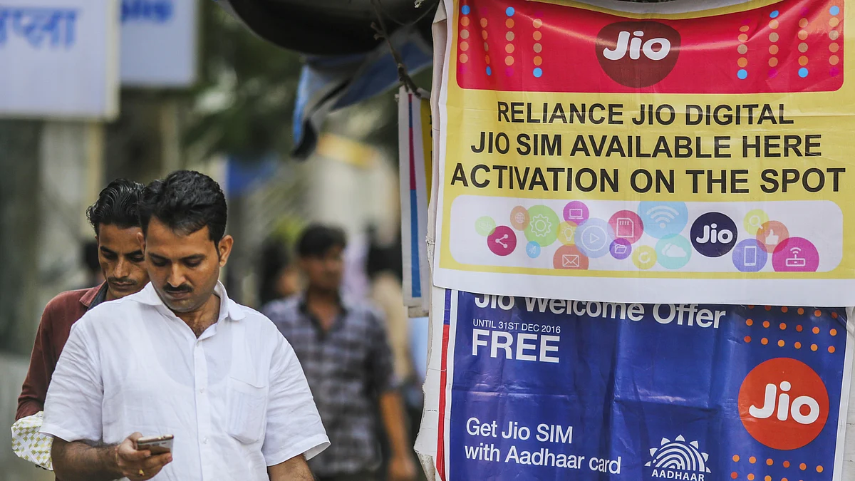 A pedestrian using a mobile phone walks past banners for Reliance Jio. (Photographer: Dhiraj Singh/Bloomberg)