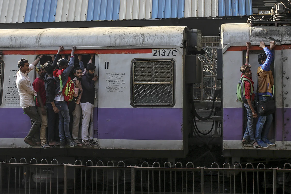 Passengers stand in the doorway, left, and on the side of train carriages as they travel by rail in Mumbai. (Photographer: Dhiraj Singh/Bloomberg)