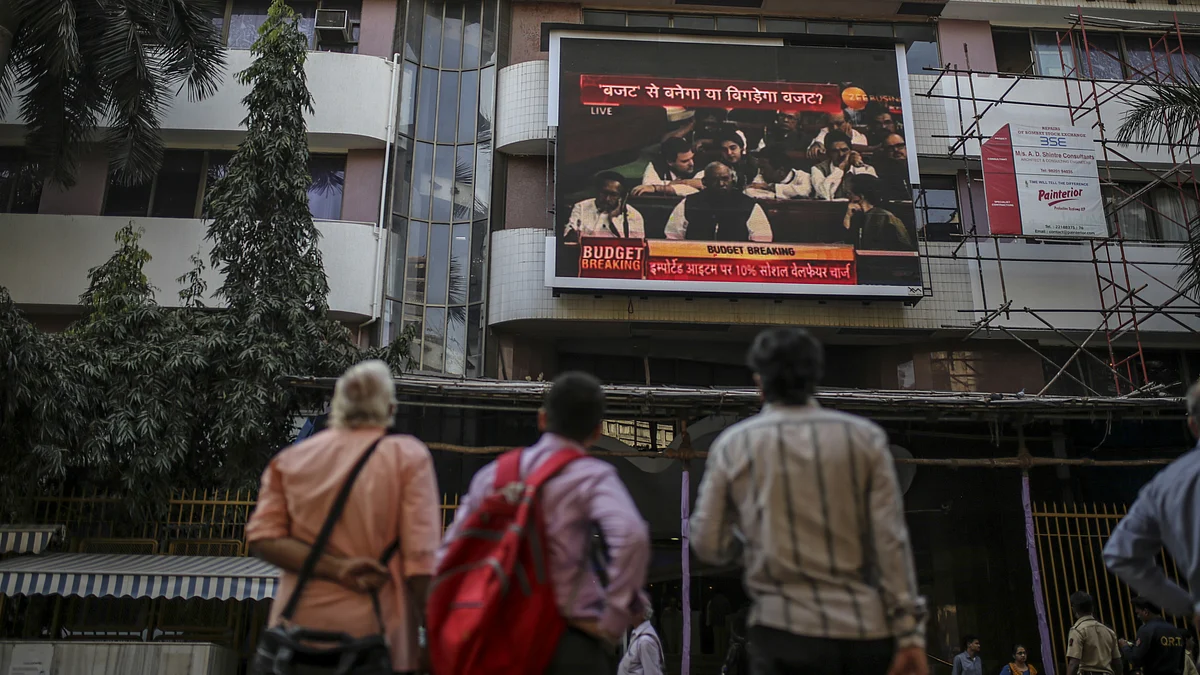 Pedestrians look up at an electronic ticker board showing a budget news report outside the Bombay Stock Exchange (BSE) in Mumbai. (Photographer: Dhiraj Singh/Bloomberg)