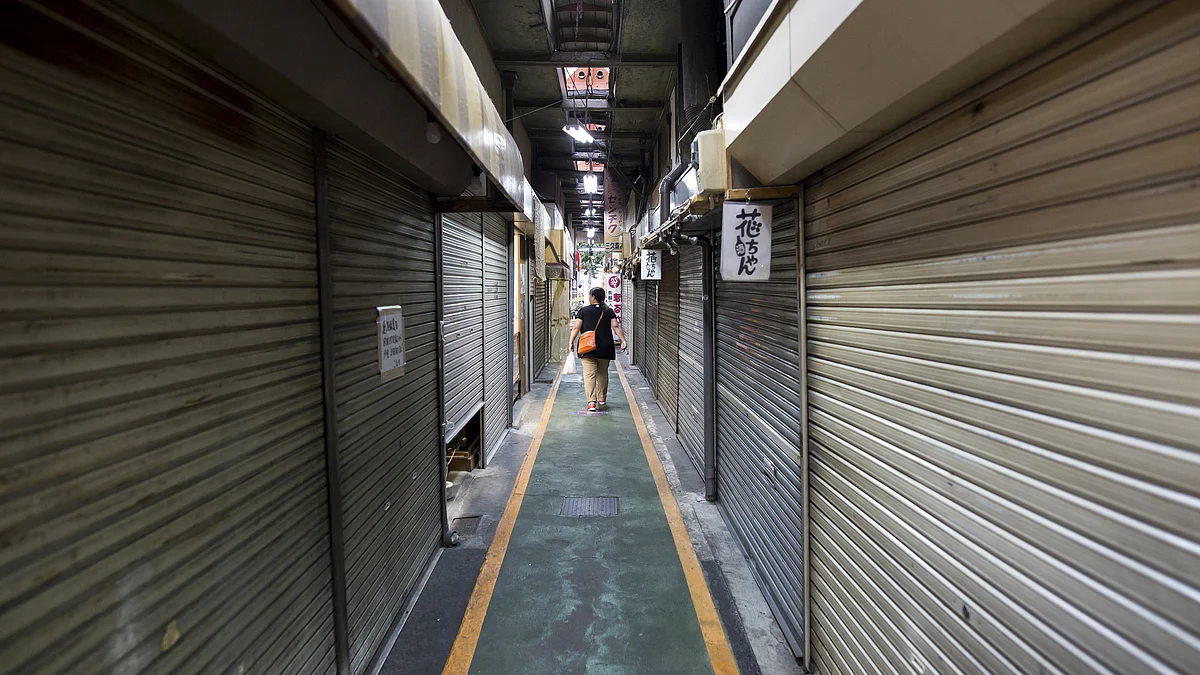 A woman walks past shuttered stores in a shopping street (Photographer: Tomohiro Ohsumi/Bloomberg)