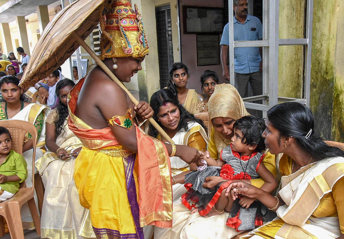 An artist dresses up as Mahabali King Maveli shakes hands with a child during ‘Onam’ celebrations at a flood relief camp in Kochi on Saturday, Aug 25, 2018. (Source: PTI)