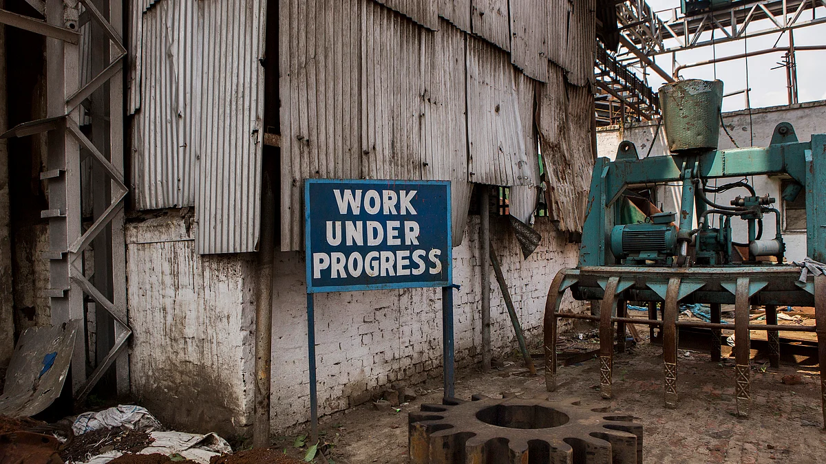 Machinery components sit around a sign reading ‘Work Under Progress’ on a factory floor. (Photographer: Prashanth Vishwanathan/Bloomberg)