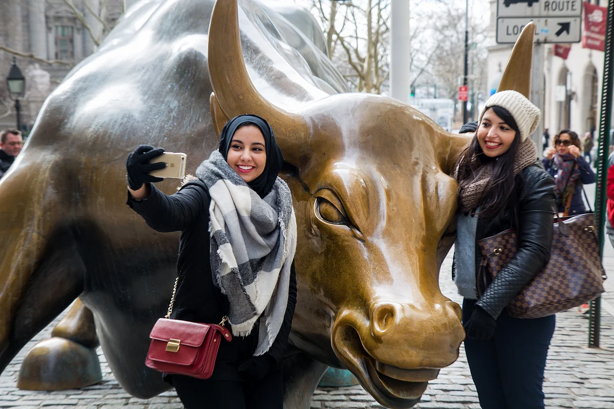 Tourists pose for pictures with the famous bull sculpture near Wall Street in New York. (Photographer: Michael Nagle/Bloomberg)