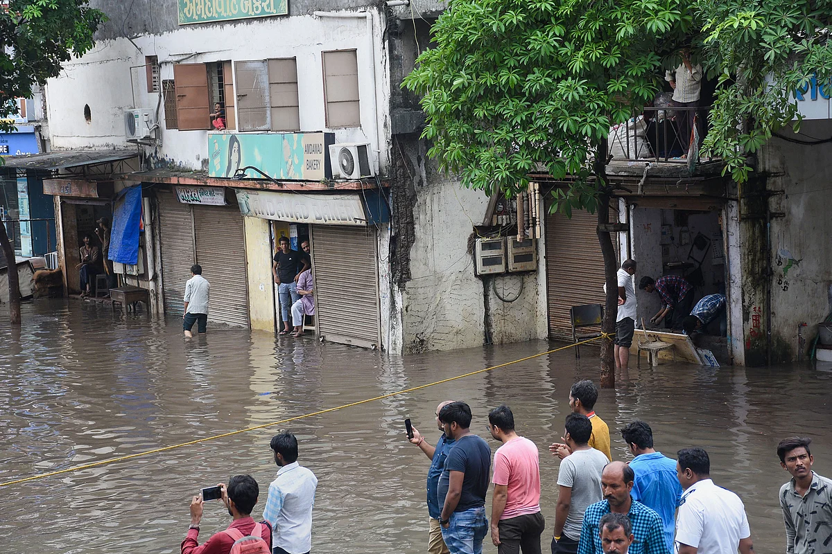 People look on at a waterlogged street where floodwater spilled out of the drainage line following heavy monsoon rainfall, in Surat. (Source: PTI)