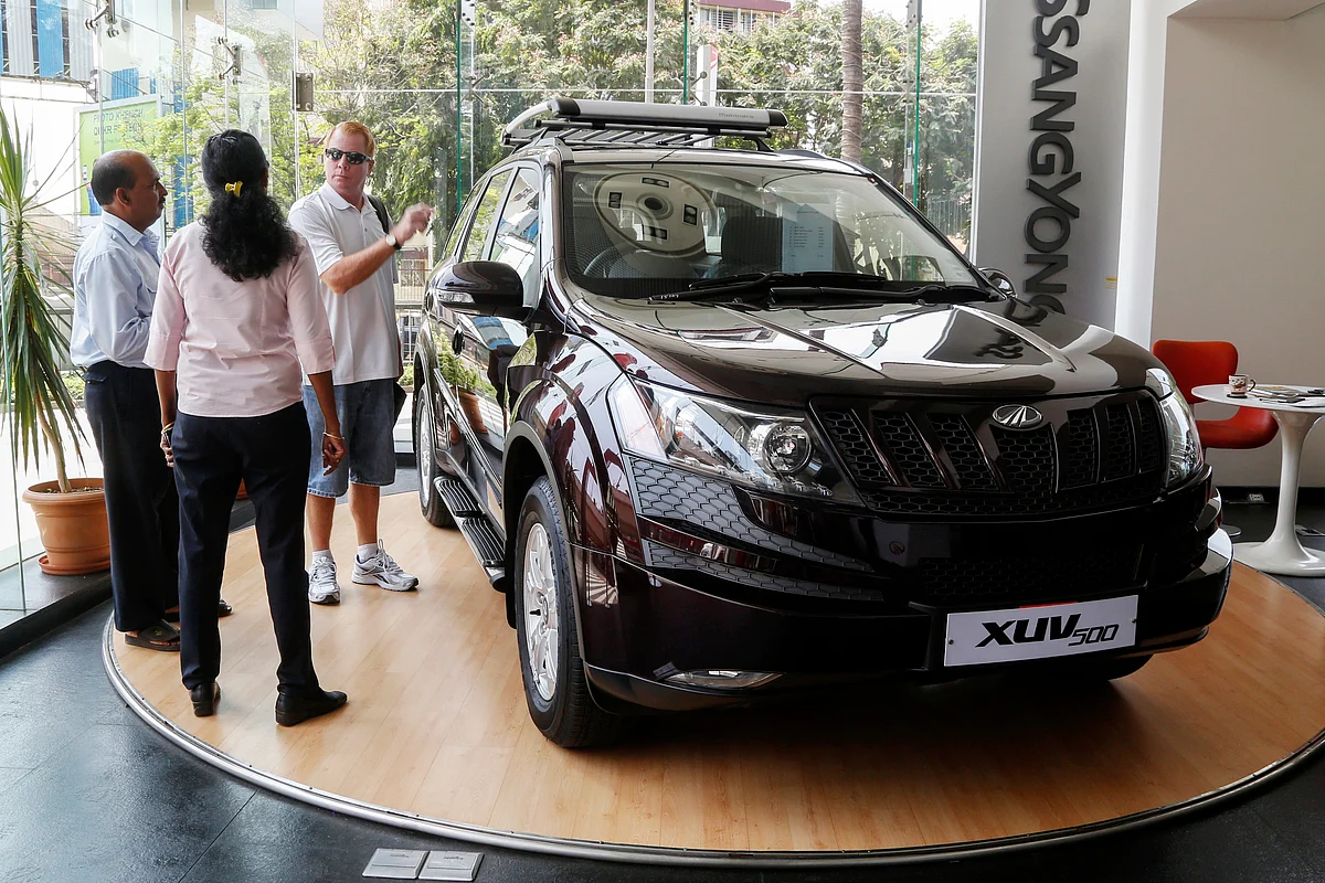 Sales assistants talk to a customer as he looks at a Mahindra XUV500 sports utility on display at a dealership in Mumbai.(Photographer: Vivek Prakash/Bloomberg)